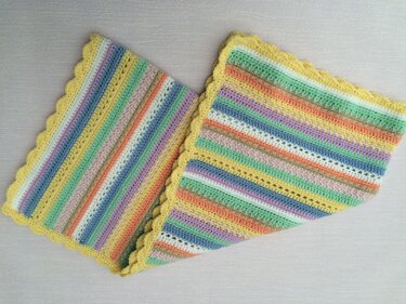 Gehäkelte Babydecke mit pastellfarbenen Streifen und gelbem Muschelrand, gefaltet