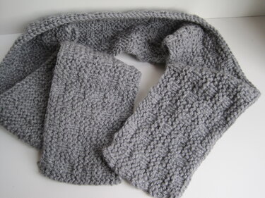 Grauer gestrickter Schal mit strukturiertem Muster auf hellem Hintergrund