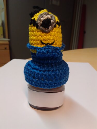 Gehäkelter gelber Überzug mit blauem Kragen auf einem Glas.