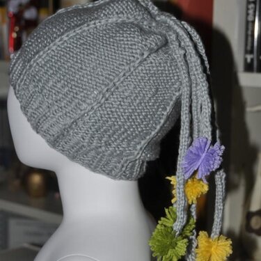 Grau gestrickte Slouch-Mütze mit langen Kordeln und bunten Bommeln auf einem Mannequin-Kopf