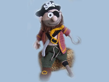 Amigurumi pirate doll with skull hat, eye patch, hook hand, and peg leg on a woven stool.