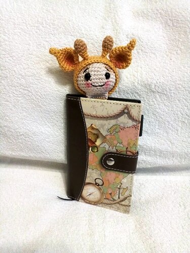 Kleines gehäkeltes Giraffenköpfchen ragt aus einem Notizbuch mit Weltkarten-Einband