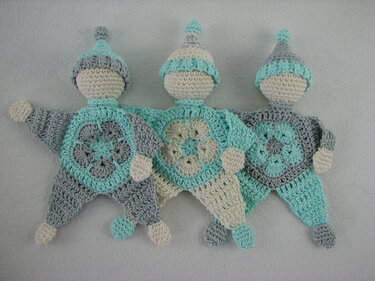 Drei gehäkelte Babyschmusetücher mit sternförmigem Körper und Mütze in Mint, Grau und Creme.