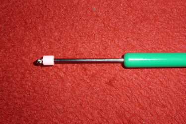 Handarbeitsnadel mit grünem Griff und rosa Stopper auf rotem Stoff