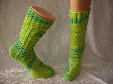 Zwei wadenhohe, grüne Stricksocken mit Zopfmuster auf einem Beinmodell