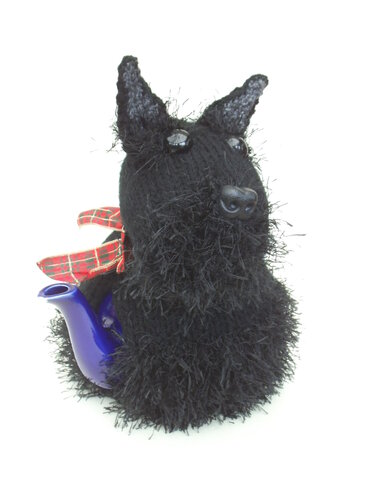 Black knitted Scottish Terrier tea cozy with a red tartan bow covering a blue teapot on a white background.