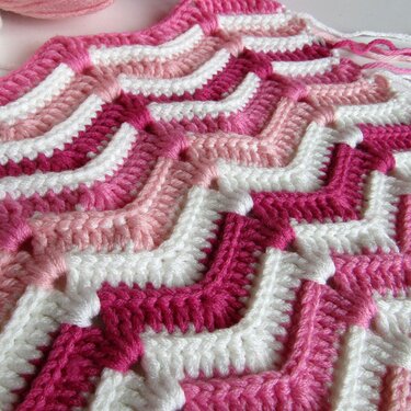 Detailaufnahme einer gehäkelten Babydecke mit Zickzackstreifen in Rosa und Weiß