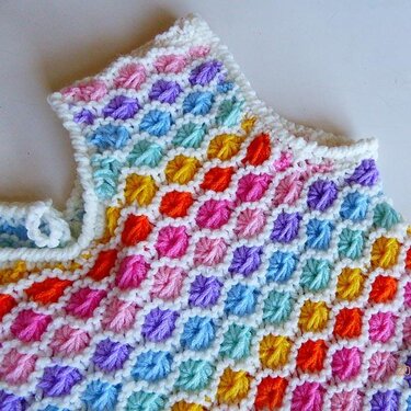 Nahaufnahme eines gestrickten Babyoberteils mit bunten Noppenmaschen und weißer Kante