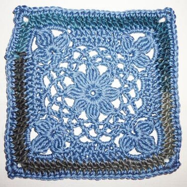 Gehäkeltes Granny Square in Blau und Grau mit zentralem Blumenstern und Eckblüten