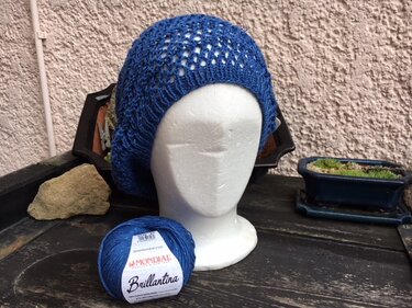 Gestricktes blaues Barett mit Lochmuster auf Schaufensterkopf, Garnknäuel daneben