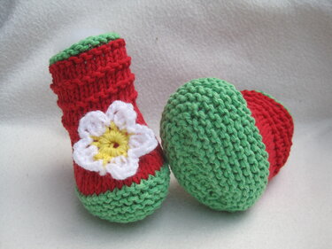 Handgestrickte Babyschuhe rot mit grünen Bündchen und weißer Blüte
