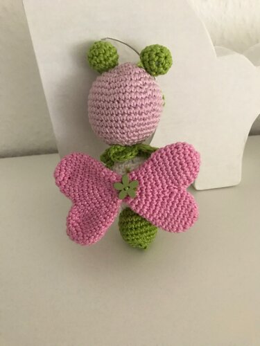 Gehäkeltes Schmetterling-Amigurumi mit rosa Flügeln, grünem Körper und Blumenknopf