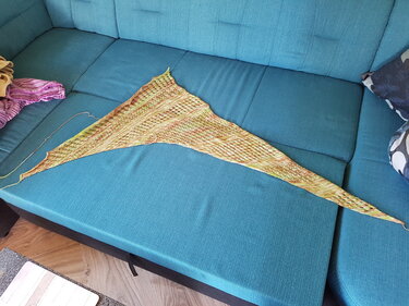 Langes asymmetrisches gestricktes Dreieckstuch in Gelb-Grün mit offenem Lochmuster auf türkisfarbenem Sofa