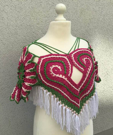 Dreieckiger gehäkelter Damenponcho mit pink-grünem Herzmuster und weißen Fransen auf Schaufensterpuppe
