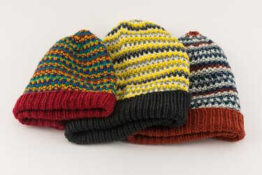 Drei farbige, gestrickte Mützen mit umgeschlagenem Rand und unterschiedlichen Mustern auf hellem Hintergrund.