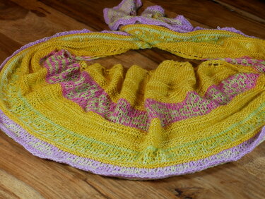 Halbrundes gestricktes Tuch in Gelb mit pastellfarbenen Streifen und Lochmuster, auf Holzboden drapiert