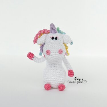 White crochet amigurumi unicorn with pastel curly mane, lilac horn and pink snout and hooves on white background