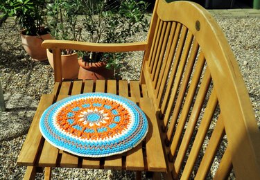 Rundes gehäkeltes Kissen in Orange, Türkis, Weiß und Grau mit Mandala-Muster auf einem Holzstuhl