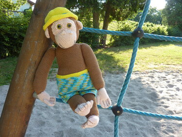 Gehäkelter Amigurumi-Affe mit gelbem Hut und bunten Shorts auf Kletternetz