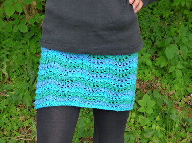 Gestrickter kurzer Rock in Blau- und Grüntönen mit Loch- und Wellenmuster über dunklen Leggings