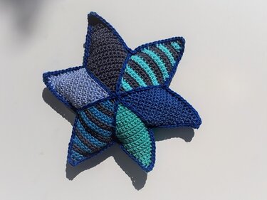 Weicher gehäkelter Stern im Patchwork aus Blau- und Türkistönen auf hellem Untergrund