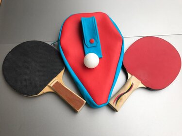 Rote und hellblaue genähte Schlägerhülle mit zwei Tischtennisschlägern und weißem Ball auf grauem Untergrund
