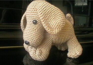 Beigefarbener gehäkelter Amigurumi-Hund mit Schlappohren und Knopfaugen auf dunklem Hintergrund