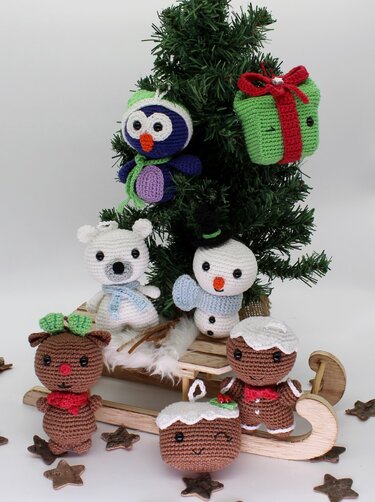 Handgehäkelte Amigurumi-Weihnachtsfiguren: Vogel, Geschenk, Eisbär, Schneemann, Rentier, Puddings und Lebkuchenmann an kleinem Tannenbaum und Schlitten