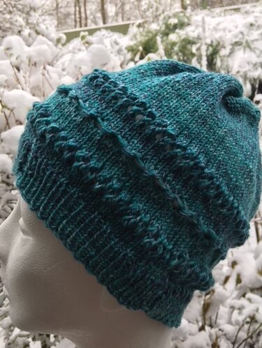 Türkisfarbene gestrickte Kinder-Beanie auf Schaufensterkopf vor verschneiter Kulisse