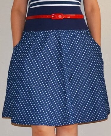 Dunkelblauer A-Linien-Rock mit weißen Punkten, rotem Gürtel und Händen in den Taschen
