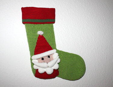 Grüner gehäkelter Weihnachtsstrumpf mit rotem Umschlag und aufgesetztem Nikolausgesicht
