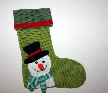 Hellgrüner gehäkelter Weihnachtsstrumpf mit Schneemann-Applikation, schwarzem Zylinder und gestreiftem Schal.