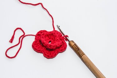 Rote Häkelblume in Arbeit mit Holzhäkelnadel und Garn