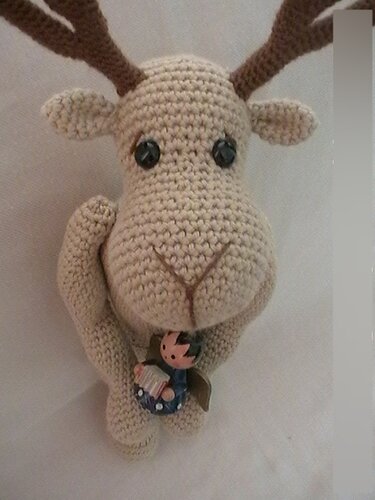 Gehäkeltes beiges Rentier-Amigurumi mit braunen Geweihen und kleiner Deko-Figur an der Vorderseite