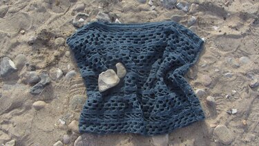 Dunkelblaues Damen-Häkelshirt mit Lochmuster auf sandigem Boden und Kieselsteinen