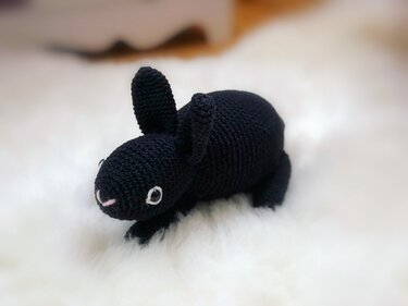 Schwarzer, gehäkelter Amigurumi-Hase auf weißem Fell