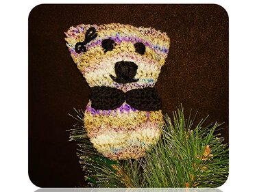 Kompakter gehäkelter Amigurumi-Teddy aus mehrfarbigem Pastellgarn mit gestickter Nase und schwarzer Fliege