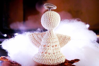 Rückansicht eines cremefarbenen Häkelengels mit Flügeln und Heiligenschein auf weißer Watte