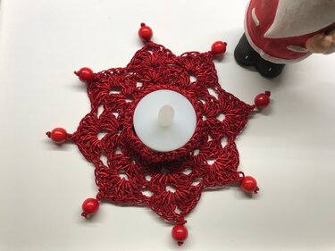 Roter gehäkelter Stern-Untersetzer mit roten Perlen und weißem batteriebetriebenem Teelicht in der Mitte.