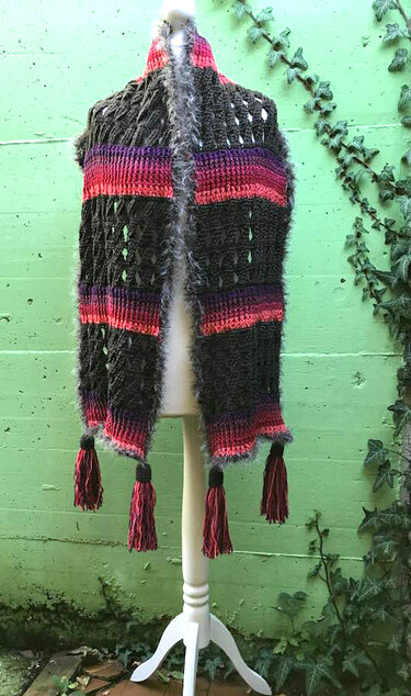Dunkelgrauer Schal mit Lochmuster, pinken und violetten Streifen, flauschigem Rand und Quasten auf einem Mannequin