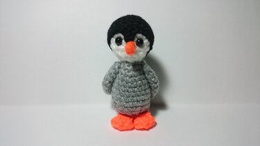 Gehäkelter Amigurumi-Pinguin mit schwarzem Kopf, weißem Gesicht, orangefarbenem Schnabel und Füßen