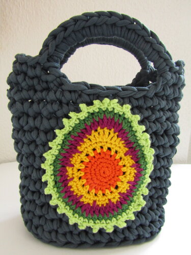 Dunkelgraue gehäkelte Tasche mit zwei Henkeln und runder, bunter Mandala-Applikation.