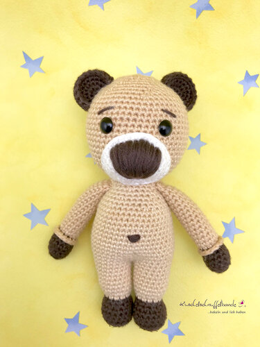 Stehender gehäkelter Teddybär in Beige mit braunen Pfoten vor gelbem Hintergrund mit Sternen