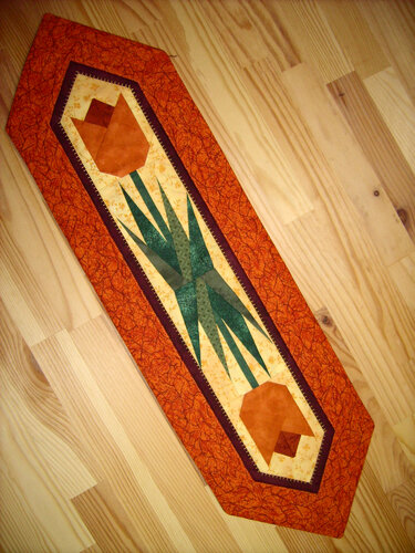 Schmaler Quilt-Tischläufer mit Tulpenmustern, orangefarbenem Rand und grünen Blättern auf Holzboden
