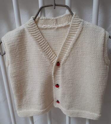 Cremefarbene gestrickte Kinderweste mit V-Ausschnitt und drei roten Knöpfen auf einem Bügel