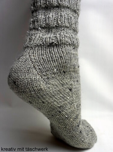 Gestrickte graue Socke mit Rippenbündchen; Detailansicht von Ferse und Schaft.