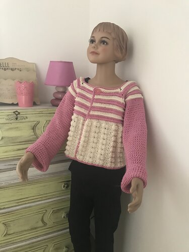 Mannequin trägt gehäkelte Kinderjacke in Rosa und Creme mit Streifen und Bobbelmuster.