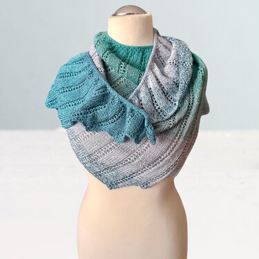 Gestrickter Drachenschwanz-Schal auf Büste, Farbverlauf Türkis zu Grau mit Lochmuster und wellenförmiger Kante.