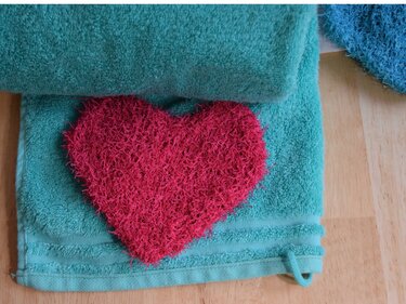 Flauschiges rosa gestricktes Herz auf einem türkisfarbenen Handtuch