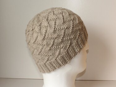 Beige Strickmütze mit Rautenmuster auf weißem Schaufensterkopf, seitliche Ansicht.